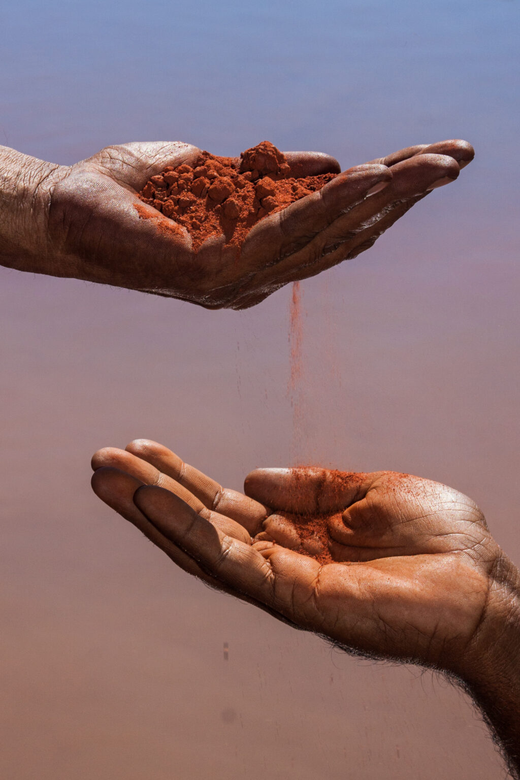 Hands holding and passing red ochre earth